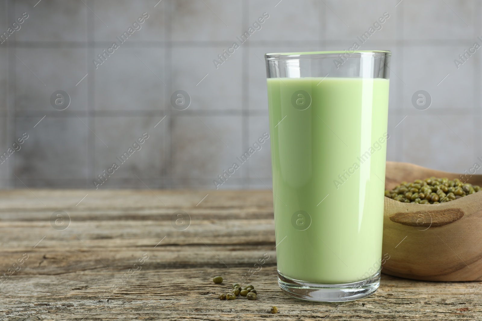 Fresh mung bean juice in glass and seeds on wooden table against grey tiled wall, closeup. Space for text Photo of Fresh mung bean juice in glass and seeds on wooden table against grey tiled wall, closeup. Space for text