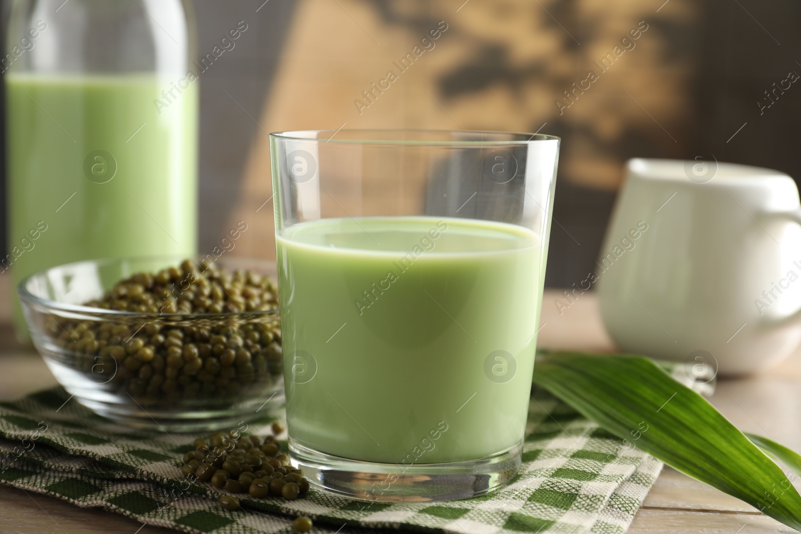 Fresh mung bean juice in glass, milk, leaves and seeds on wooden table, closeup Photo of Fresh mung bean juice in glass, milk, leaves and seeds on wooden table, closeup