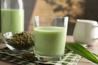 Photo of Fresh mung bean juice in glass, milk, leaves and seeds on wooden table, closeup