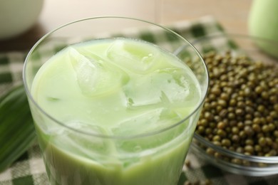 Photo of Fresh mung bean juice with ice in glass and seeds on table, closeup