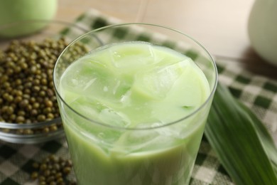Photo of Fresh mung bean juice with ice in glass and seeds on table, closeup