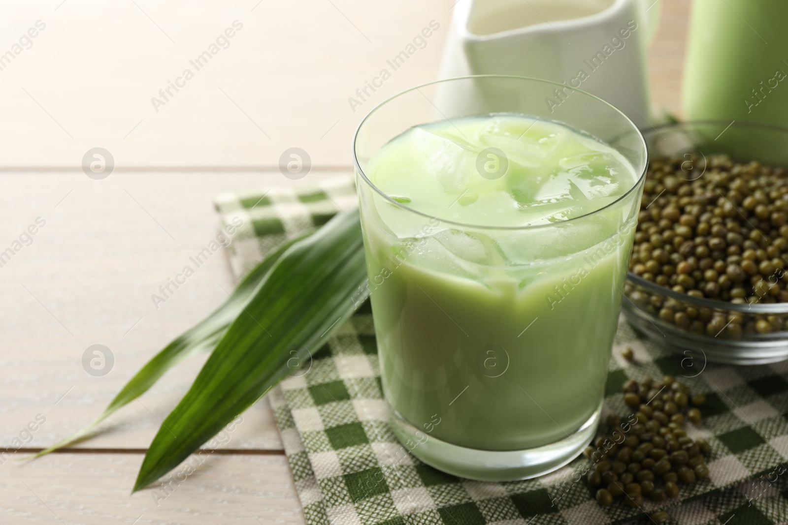 Fresh mung bean juice with ice in glass, leaves and seeds on wooden table, closeup Photo of Fresh mung bean juice with ice in glass, leaves and seeds on wooden table, closeup