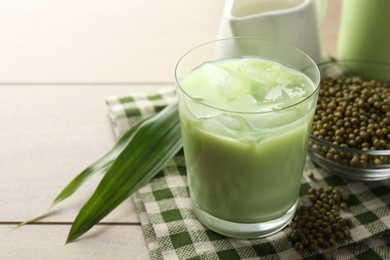 Photo of Fresh mung bean juice with ice in glass, leaves and seeds on wooden table, closeup