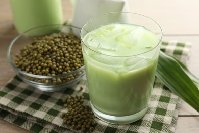 Photo of Fresh mung bean juice with ice in glass, leaves and seeds on wooden table, closeup