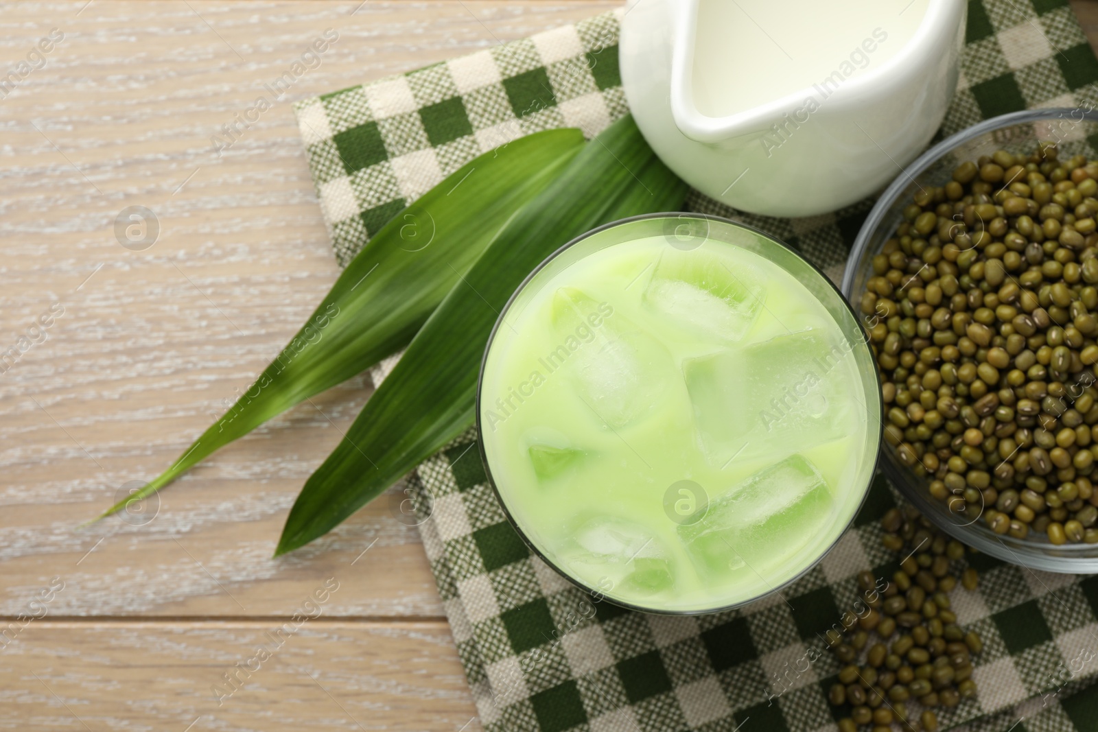 Fresh mung bean juice with ice in glass, milk, leaves and seeds on wooden table, flat lay Photo of Fresh mung bean juice with ice in glass, milk, leaves and seeds on wooden table, flat lay
