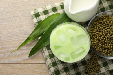 Photo of Fresh mung bean juice with ice in glass, milk, leaves and seeds on wooden table, flat lay