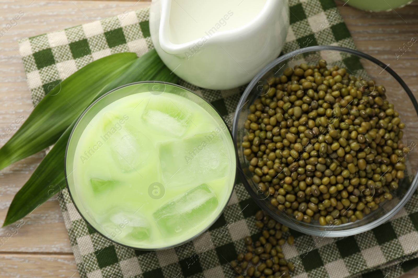 Fresh mung bean juice with ice in glass, milk, leaves and seeds on wooden table, flat lay Photo of Fresh mung bean juice with ice in glass, milk, leaves and seeds on wooden table, flat lay