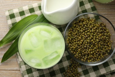 Photo of Fresh mung bean juice with ice in glass, milk, leaves and seeds on wooden table, flat lay