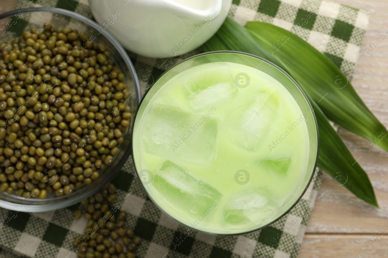 Fresh mung bean juice with ice in glass, leaves and seeds on wooden table, flat lay Photo of Fresh mung bean juice with ice in glass, leaves and seeds on wooden table, flat lay