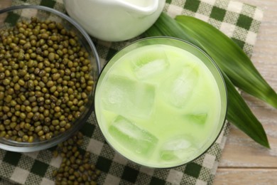 Photo of Fresh mung bean juice with ice in glass, leaves and seeds on wooden table, flat lay