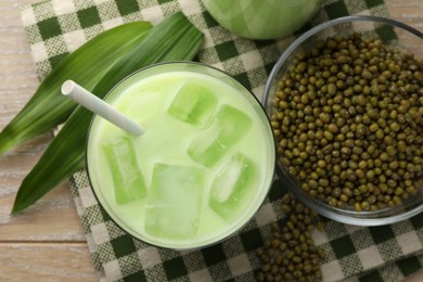 Photo of Fresh mung bean juice with ice in glass, leaves and seeds on wooden table, flat lay