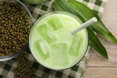 Photo of Fresh mung bean juice with ice in glass, leaves and seeds on wooden table, flat lay