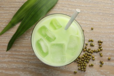 Photo of Fresh mung bean juice with ice in glass, leaves and seeds on wooden table, flat lay