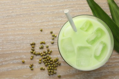 Photo of Fresh mung bean juice with ice in glass, leaves and seeds on wooden table, flat lay. Space for text