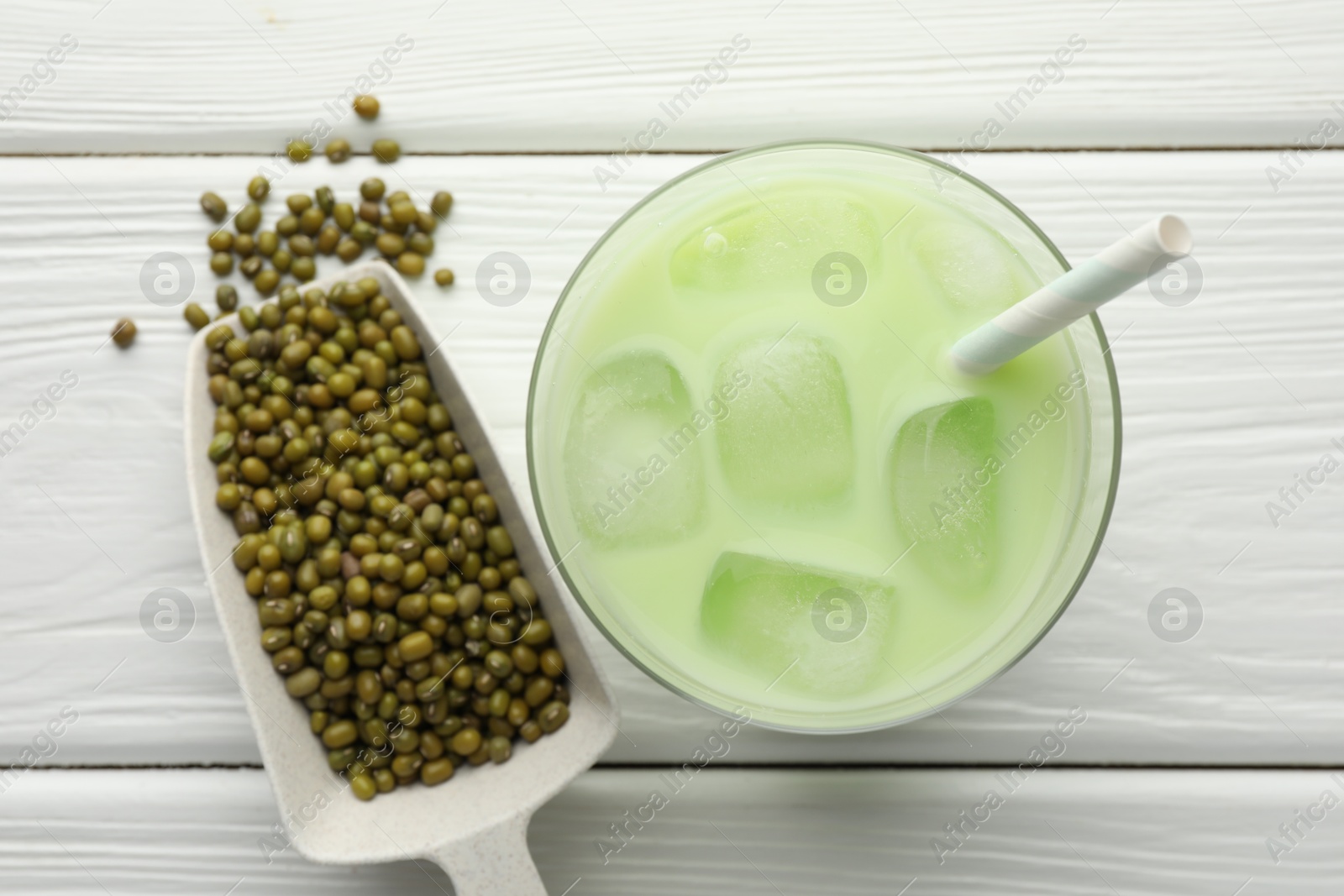Fresh mung bean juice with ice in glass and seeds on white wooden table, flat lay Photo of Fresh mung bean juice with ice in glass and seeds on white wooden table, flat lay