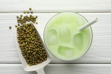 Photo of Fresh mung bean juice with ice in glass and seeds on white wooden table, flat lay