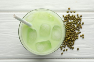 Photo of Fresh mung bean juice with ice in glass and seeds on white wooden table, flat lay