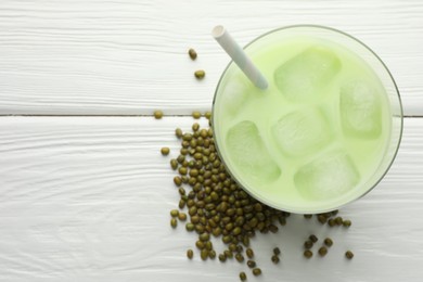 Photo of Fresh mung bean juice with ice in glass and seeds on white wooden table, flat lay. Space for text