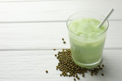 Photo of Fresh mung bean juice with ice in glass and seeds on white wooden table, closeup. Space for text