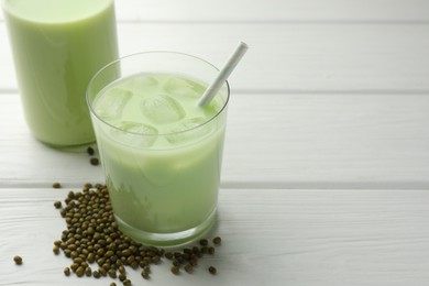Photo of Fresh mung bean juice with ice in glass and seeds on white wooden table, closeup. Space for text