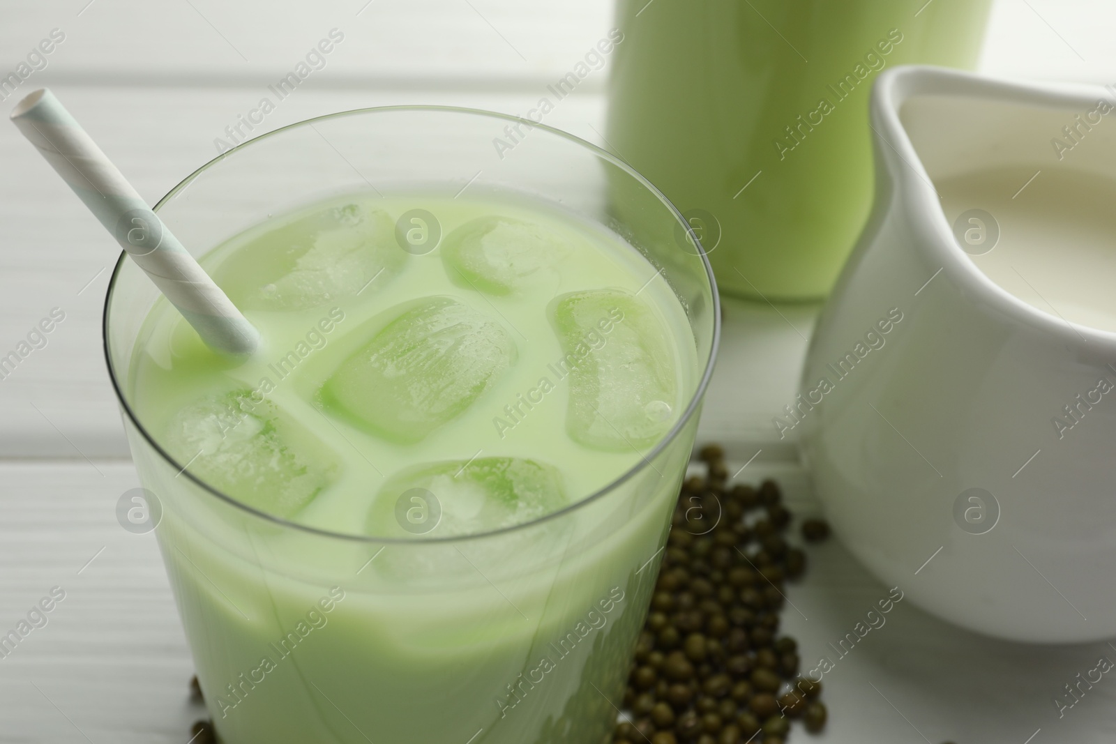 Fresh mung bean juice with ice in glass and seeds on white wooden table, closeup Photo of Fresh mung bean juice with ice in glass and seeds on white wooden table, closeup