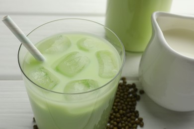 Photo of Fresh mung bean juice with ice in glass and seeds on white wooden table, closeup