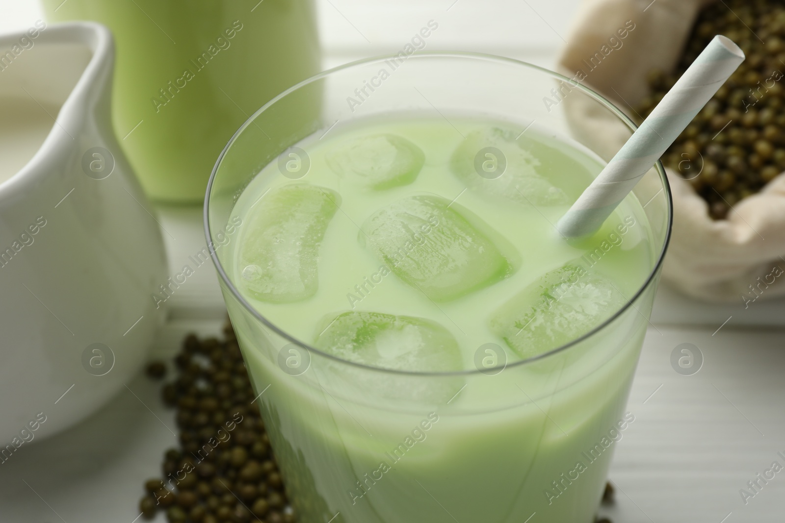 Fresh mung bean juice with ice in glass and seeds on white wooden table, closeup Photo of Fresh mung bean juice with ice in glass and seeds on white wooden table, closeup