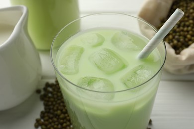 Photo of Fresh mung bean juice with ice in glass and seeds on white wooden table, closeup