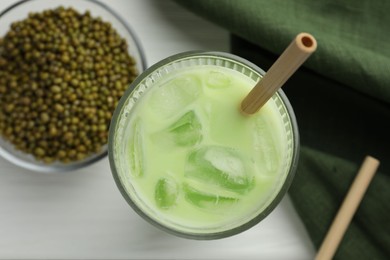 Photo of Fresh mung bean juice with ice in glass and seeds on white table, flat lay
