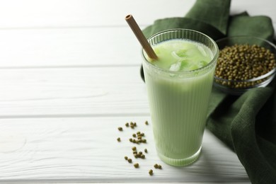 Photo of Fresh mung bean juice with ice in glass and seeds on white wooden table, closeup. Space for text