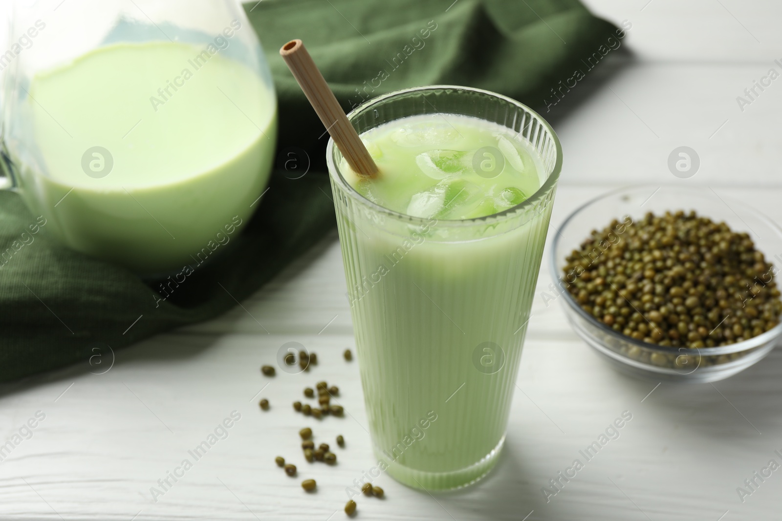 Fresh mung bean juice with ice in glass and seeds on white wooden table, closeup Photo of Fresh mung bean juice with ice in glass and seeds on white wooden table, closeup