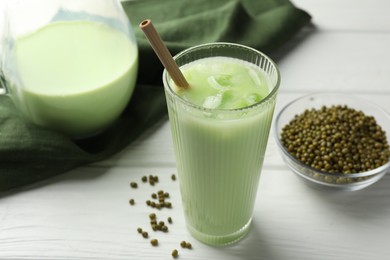 Photo of Fresh mung bean juice with ice in glass and seeds on white wooden table, closeup