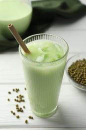 Photo of Fresh mung bean juice with ice in glass and seeds on white wooden table, closeup