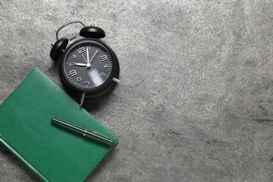 Photo of Time for knowledge. Alarm clock, notebook and pen on grey textured table, flat lay. Space for text