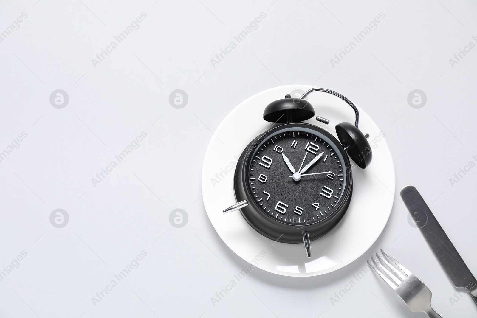 Photo of Time for meal. Alarm clock, plate and cutlery on light grey background, flat lay. Space for text