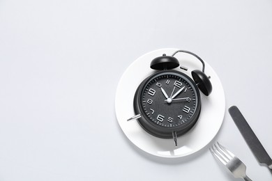 Photo of Time for meal. Alarm clock, plate and cutlery on light grey background, flat lay. Space for text