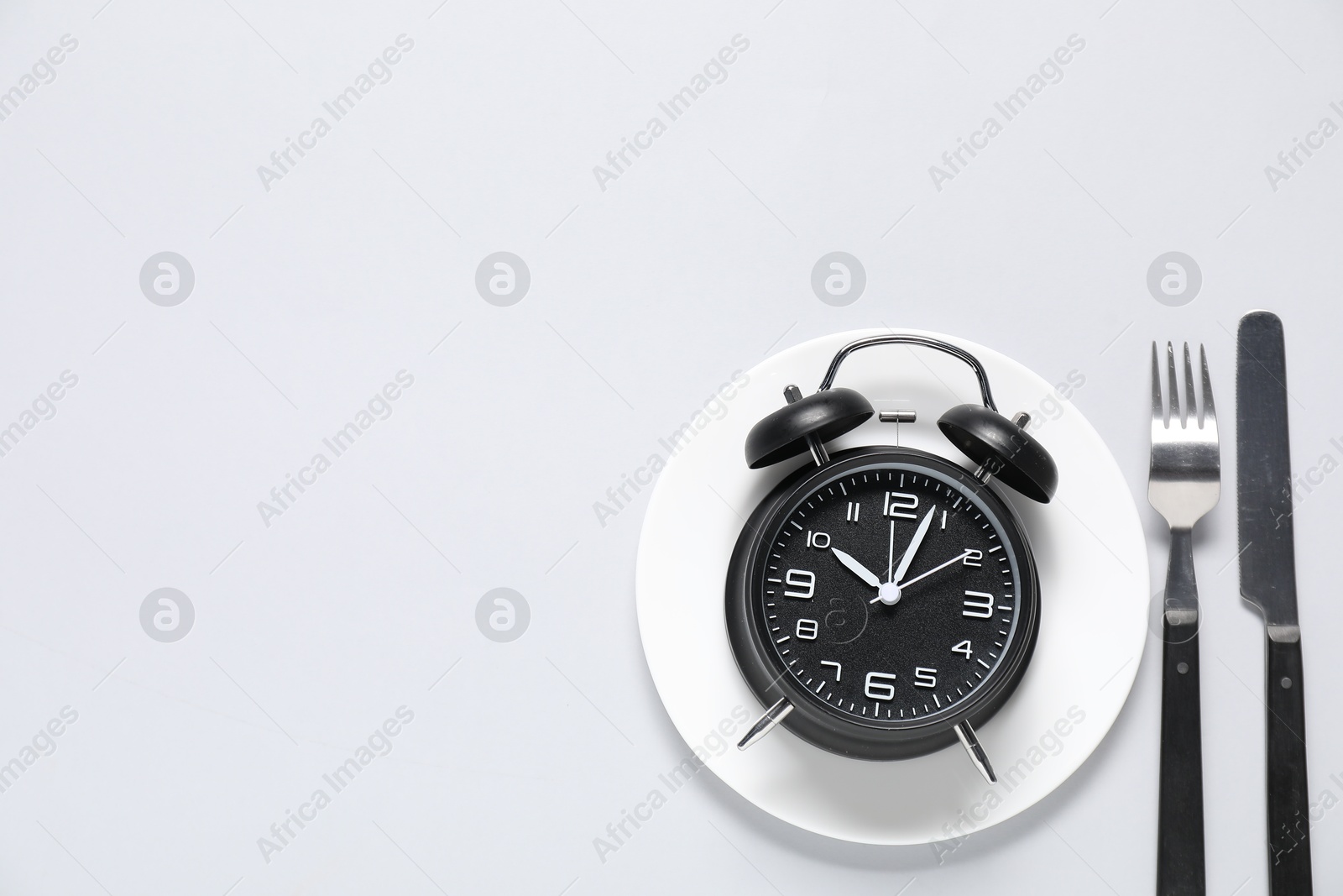 Photo of Time for meal. Alarm clock, plate and cutlery on light grey background, flat lay. Space for text