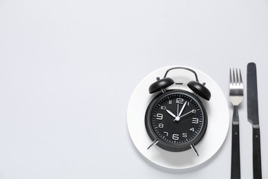 Photo of Time for meal. Alarm clock, plate and cutlery on light grey background, flat lay. Space for text