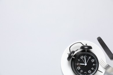 Photo of Time for meal. Alarm clock, plate and cutlery on light grey background, flat lay. Space for text