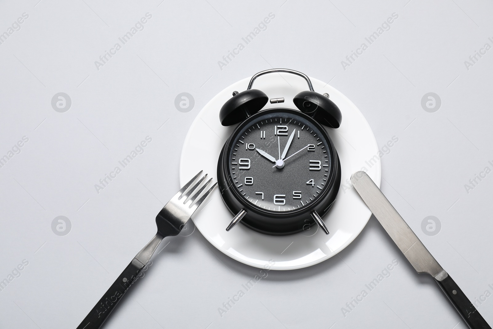 Photo of Time for meal. Alarm clock, plate and cutlery on light grey background, flat lay