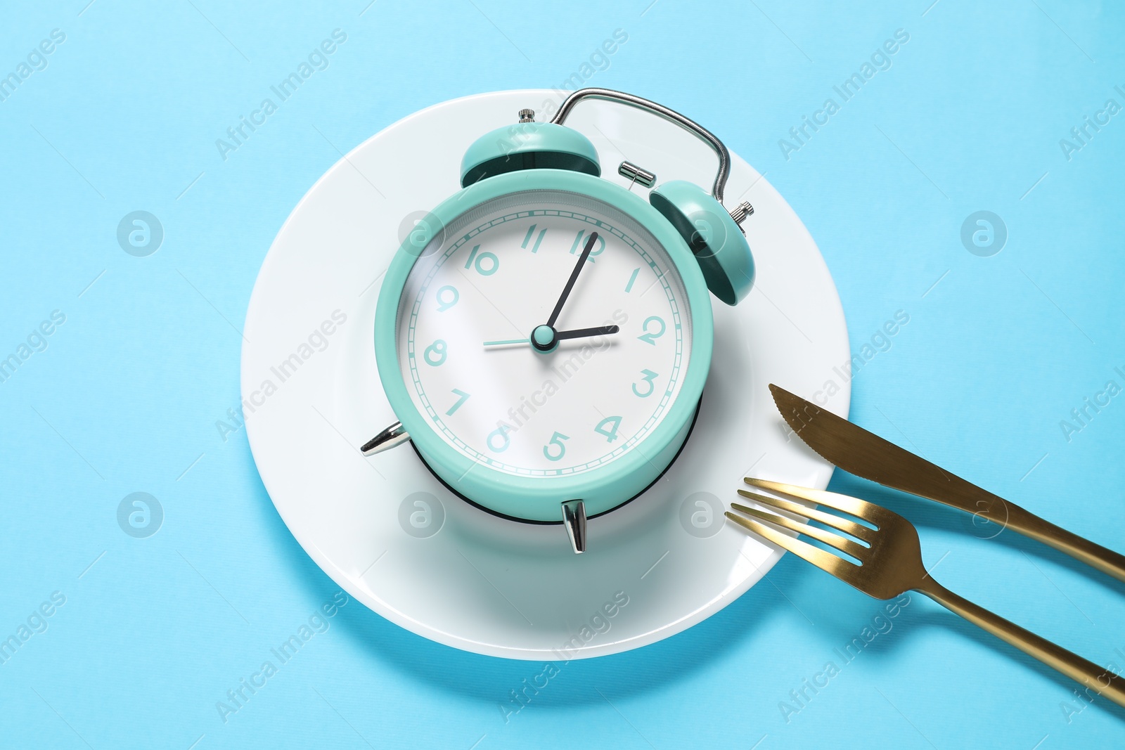 Photo of Time for meal. Alarm clock, plate and cutlery on light blue background, flat lay