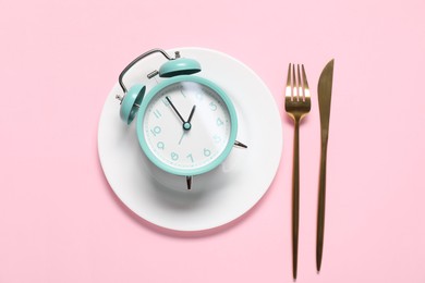 Photo of Time for meal. Alarm clock, plate and cutlery on pink background, flat lay