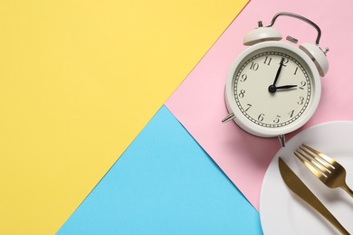 Photo of Time for meal. Alarm clock, plate and cutlery on color background, flat lay. Space for text