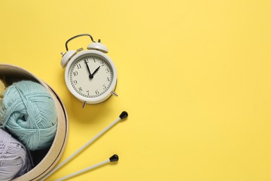 Photo of Time for hobby. Alarm clock, yarn and knitting needles on yellow background, flat lay. Space for text