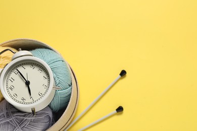 Photo of Time for hobby. Alarm clock, yarn and knitting needles on yellow background, flat lay. Space for text