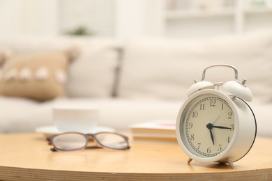 Photo of Time for knowledge. Alarm clock, glasses and books on wooden table indoors, closeup