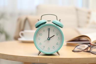 Photo of Time for knowledge. Alarm clock, glasses and books on wooden table indoors, closeup