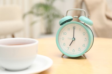 Photo of Time for tea break. Alarm clock and cup of hot drink on wooden table indoors, closeup