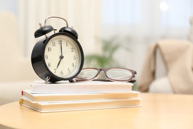 Photo of Time for knowledge. Alarm clock, glasses and books on wooden table indoors, space for text