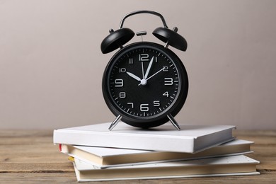 Photo of Time for knowledge. Alarm clock and books on wooden table, closeup